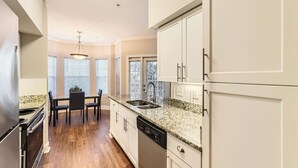 Una cocina con armarios blancos, encimeras de granito, lavavajillas y un comedor con mesa y sillas.