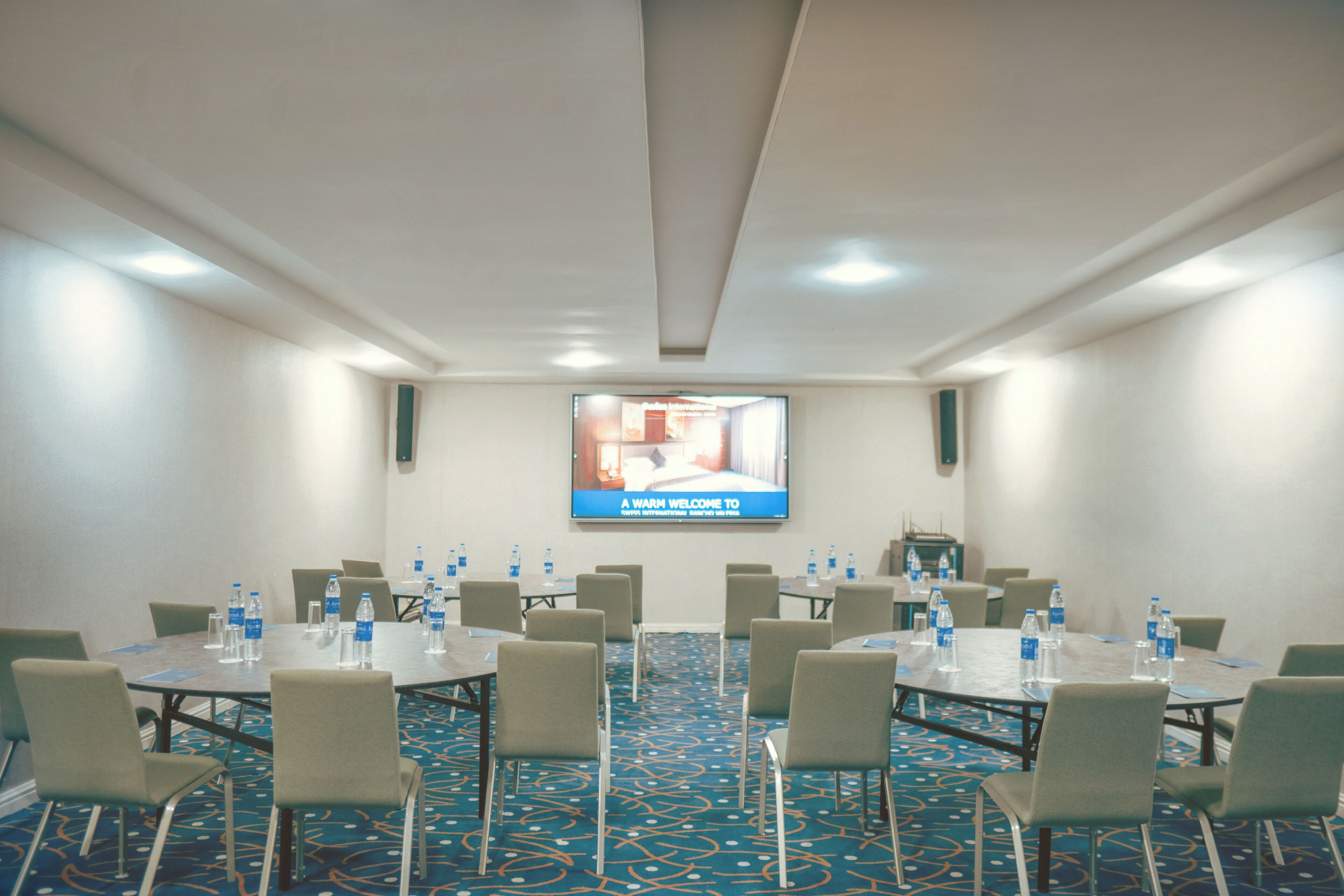 A conference room with tables, chairs, and a screen displaying a welcome message.