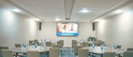 A conference room with tables, chairs, and a screen displaying a welcome message.