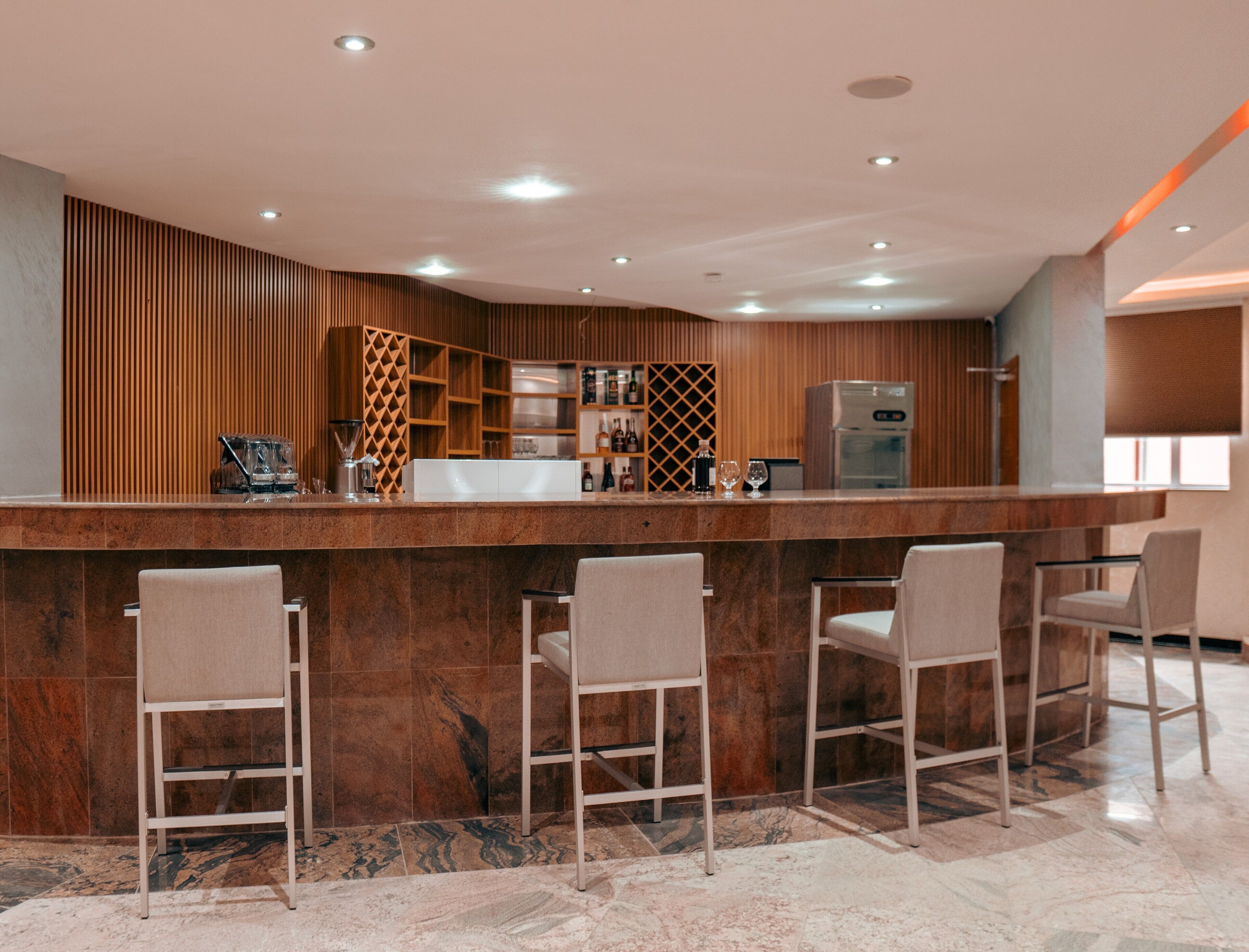 A modern bar area with a marble countertop, bar stools, and a wine rack.