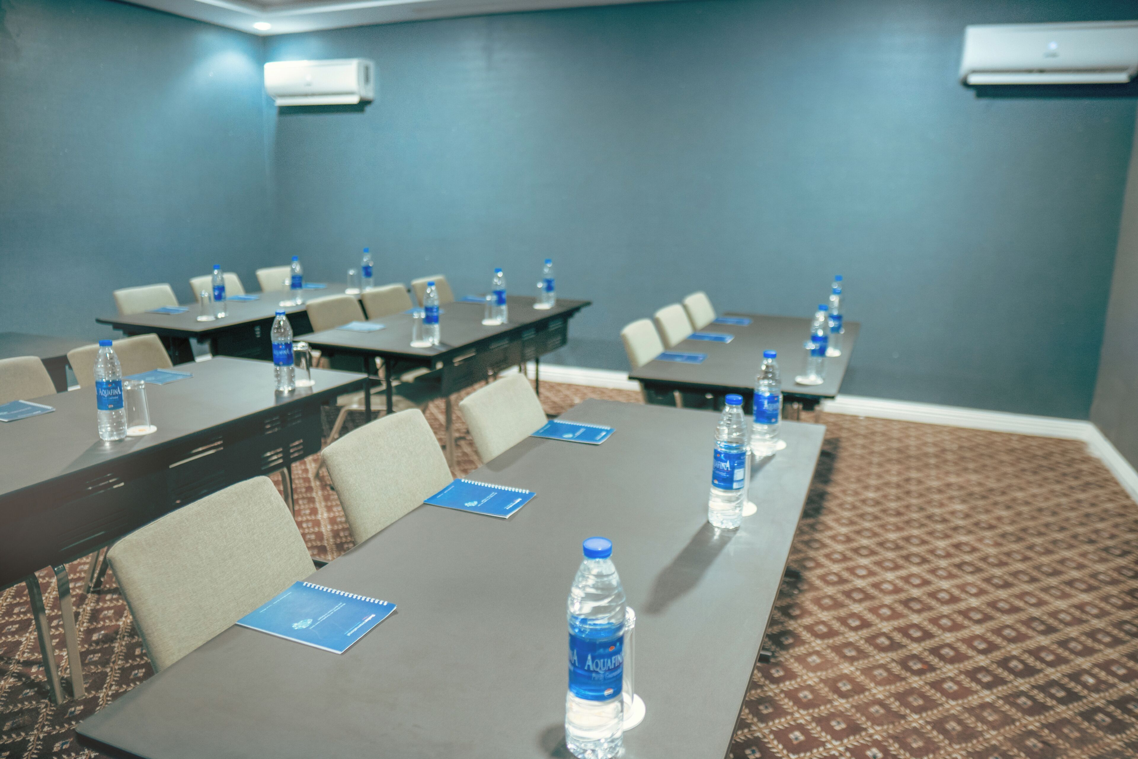 A conference room with tables, chairs, water bottles, and air conditioning units.
