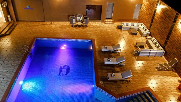 A swimming pool with a blue-lit deck, lounge chairs, and a seating area with a wooden floor. - Swiss International Rancho Valeria (Warri)