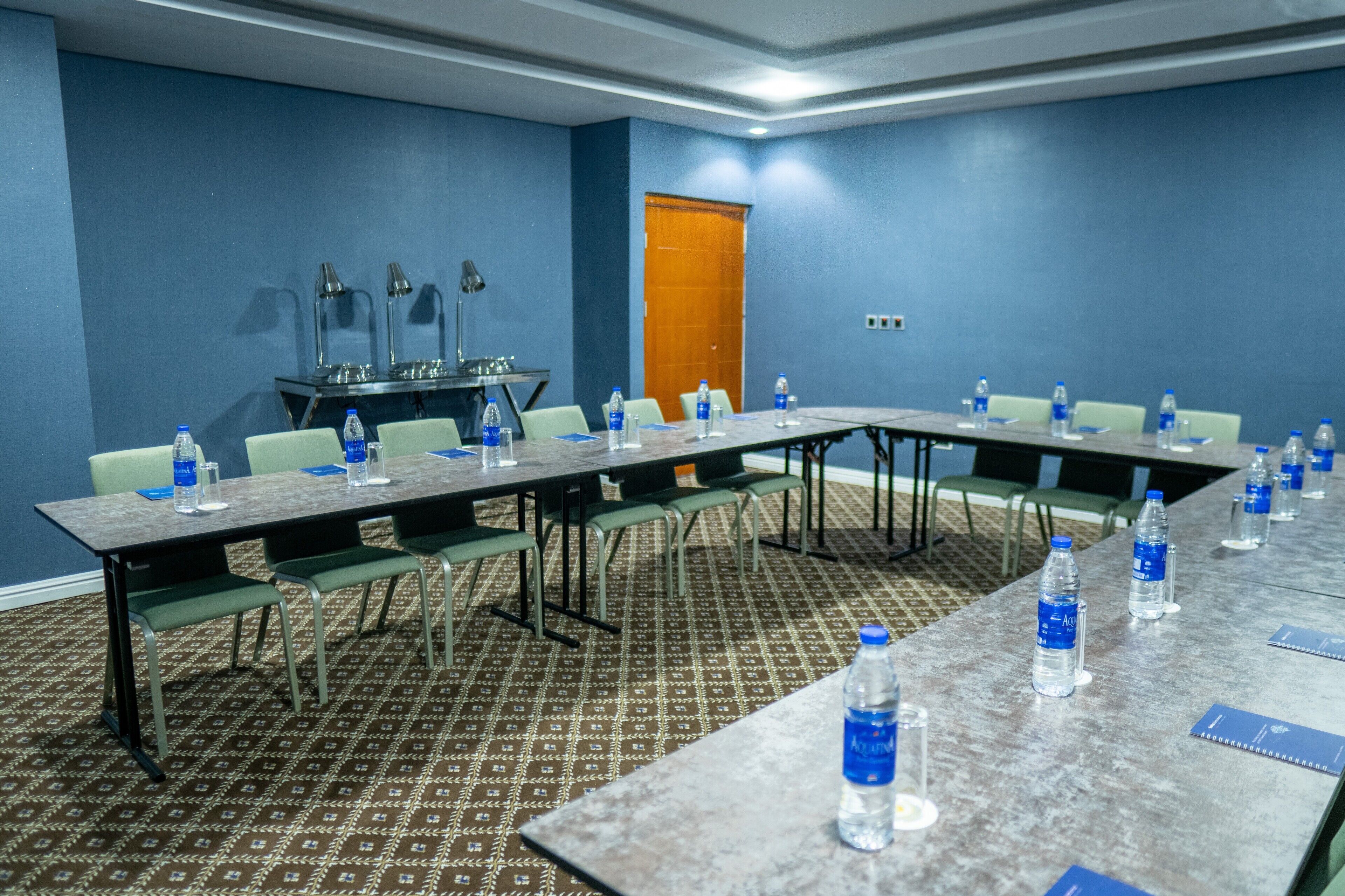 A conference room with a long table, chairs, water bottles, and a door.