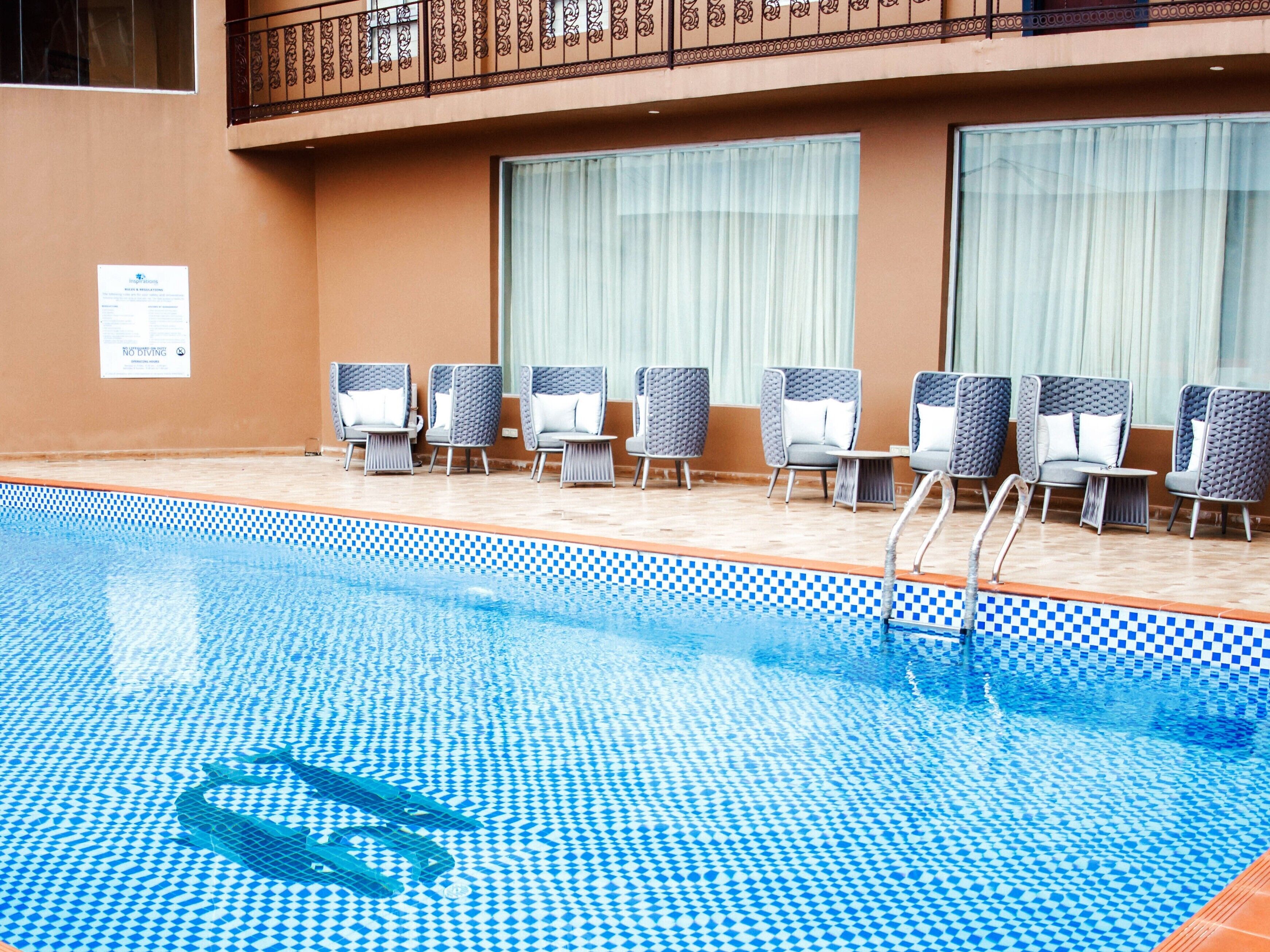 A swimming pool with checkered tiles, lounge chairs, and a balcony with ornate railings.