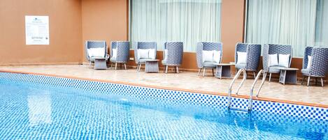 A swimming pool with checkered tiles, lounge chairs, and a balcony with ornate railings.