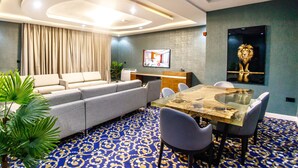 A modern hotel room with a sofa, a dining table with chairs, a TV, and a lion painting on the wall. - Swiss International Rancho Valeria (Warri)