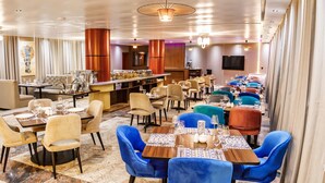 A modern restaurant with multiple dining areas, including a bar and a seating area with blue chairs. Tables are set with plates, glasses, and cutlery. - Swiss International Rancho Valeria (Warri)