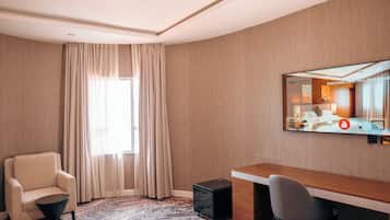 A hotel room with a large window, a desk, a chair, a small table, and a speaker.