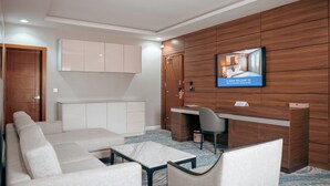 A modern hotel room with a sofa, a desk, and a television mounted on the wall. - Swiss International Rancho Valeria (Warri)