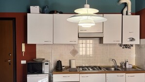 A compact kitchen with white cabinets, a microwave, a gas stove, and a round table with chairs. - VERONA EASY LOFT - ID M0230911208 (Verona)