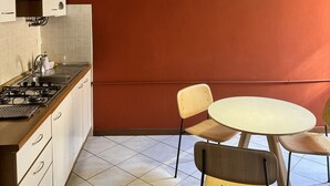 A kitchen with a gas stove, white cabinets, a red wall, a round table with chairs, and a pendant light. - VERONA EASY LOFT - ID M0230911208 (Verona)