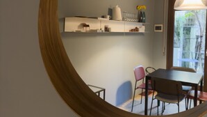 Een ronde spiegel die een eethoek weerspiegelt, met een tafel, stoelen en een plank met diverse objecten.