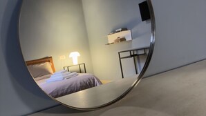 Een ronde spiegel die een kamer weerkaatst met een bed, een nachtkastje en een wandplank.