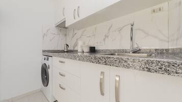 Cocina moderna con armarios blancos, encimera de granito, lavadora integrada y pileta de acero inoxidable.