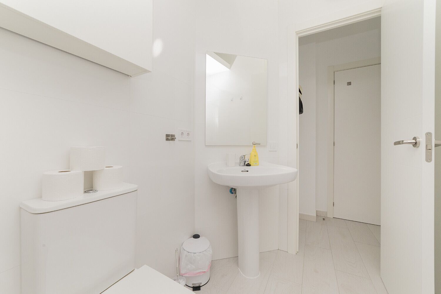 Un baño moderno con lavamanos blanco, soporte para papel higiénico y espejo.