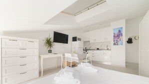 Ein modernes Hotelzimmer mit einem großen Bett, einem Schreibtisch, einem Stuhl, einem Fernseher und einer Küchenzeile.