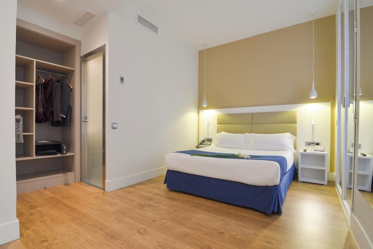 A hotel room with a bed, bedside tables, a wardrobe, and a mirror.