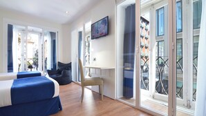 A modern hotel room with a bed, a desk, and a chair. There is a television on the wall and a balcony with a view of the city. - Hotel Miau  (Madrid)