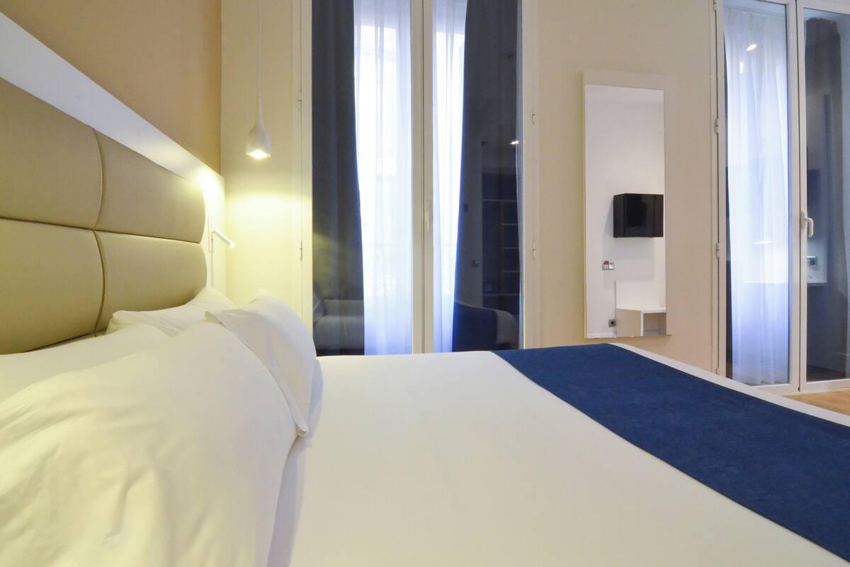 A hotel room with a large bed, a TV mounted on the wall, and a sliding glass door leading to a balcony.