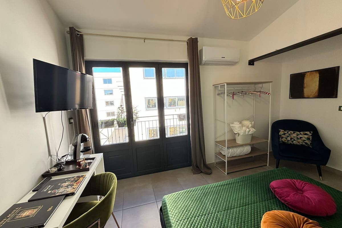 Une chambre d’hôtel comprenant un lit, une télévision, un bureau avec un ordinateur, une armoire et un balcon avec vue sur les bâtiments.