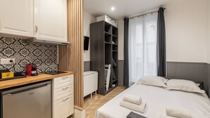 Habitación de hotel compacta con kitchenette, una cama y toallas ordenadas, armario y un amplio ventanal con cortinas.