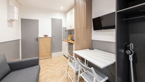 Una cocina compacta con comedor, un sofá y un televisor montado en la pared.