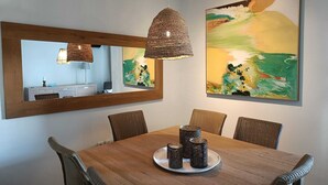 A dining area with a wooden table, wicker chairs, a mirror, and abstract paintings.