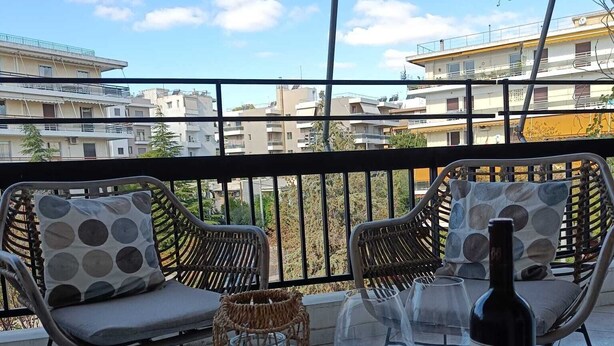 A balcony with wicker furniture, a glass table, wine glasses, and a bottle.