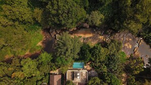 An aerial view of a resort with a swimming pool, a small building, and dense surrounding forest. - Hunters Hideout Resort (Vythiri)