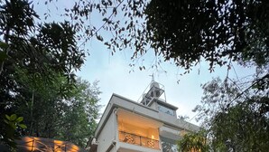 A modern two-story building with a balcony, a stone wall, and a rock feature. - Hunters Hideout Resort (Vythiri)