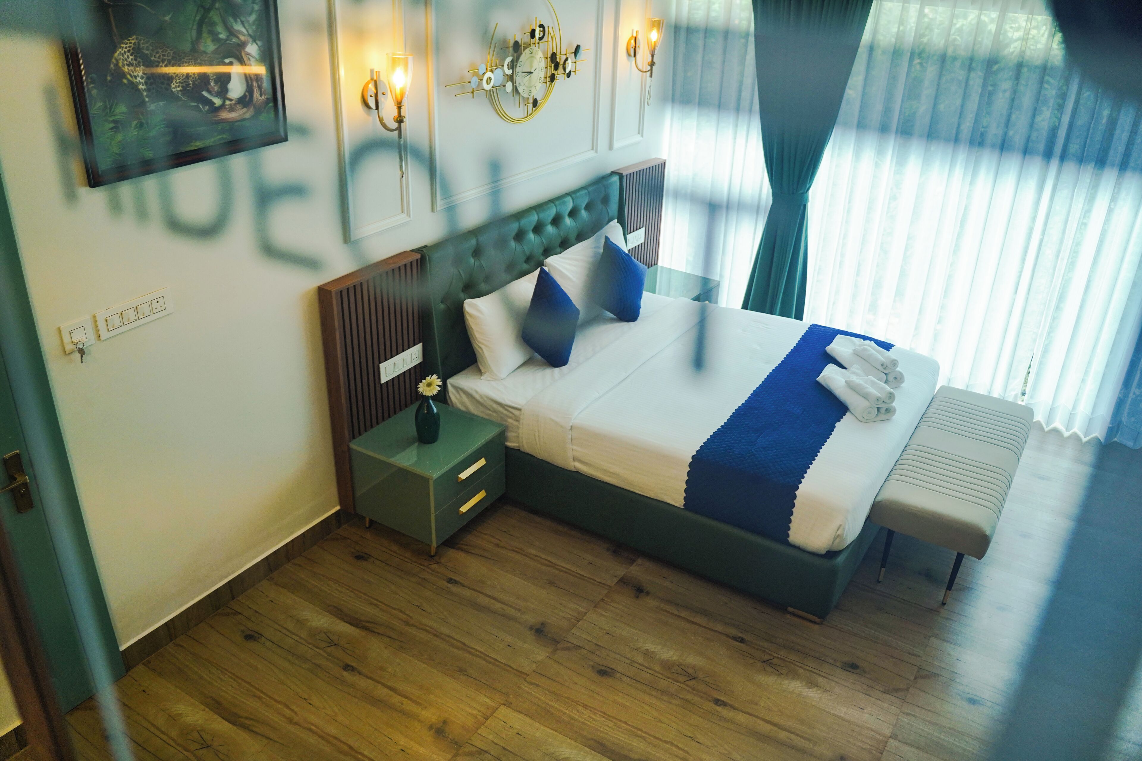 Une chambre d’hôtel bien aménagée, avec un grand lit, des tables de chevet, une petite table et une horloge murale.