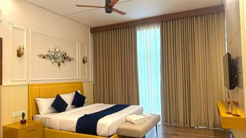 A modern bedroom with a yellow bed, a ceiling fan, a large window with curtains, a wall clock, and a small nightstand with a lamp.