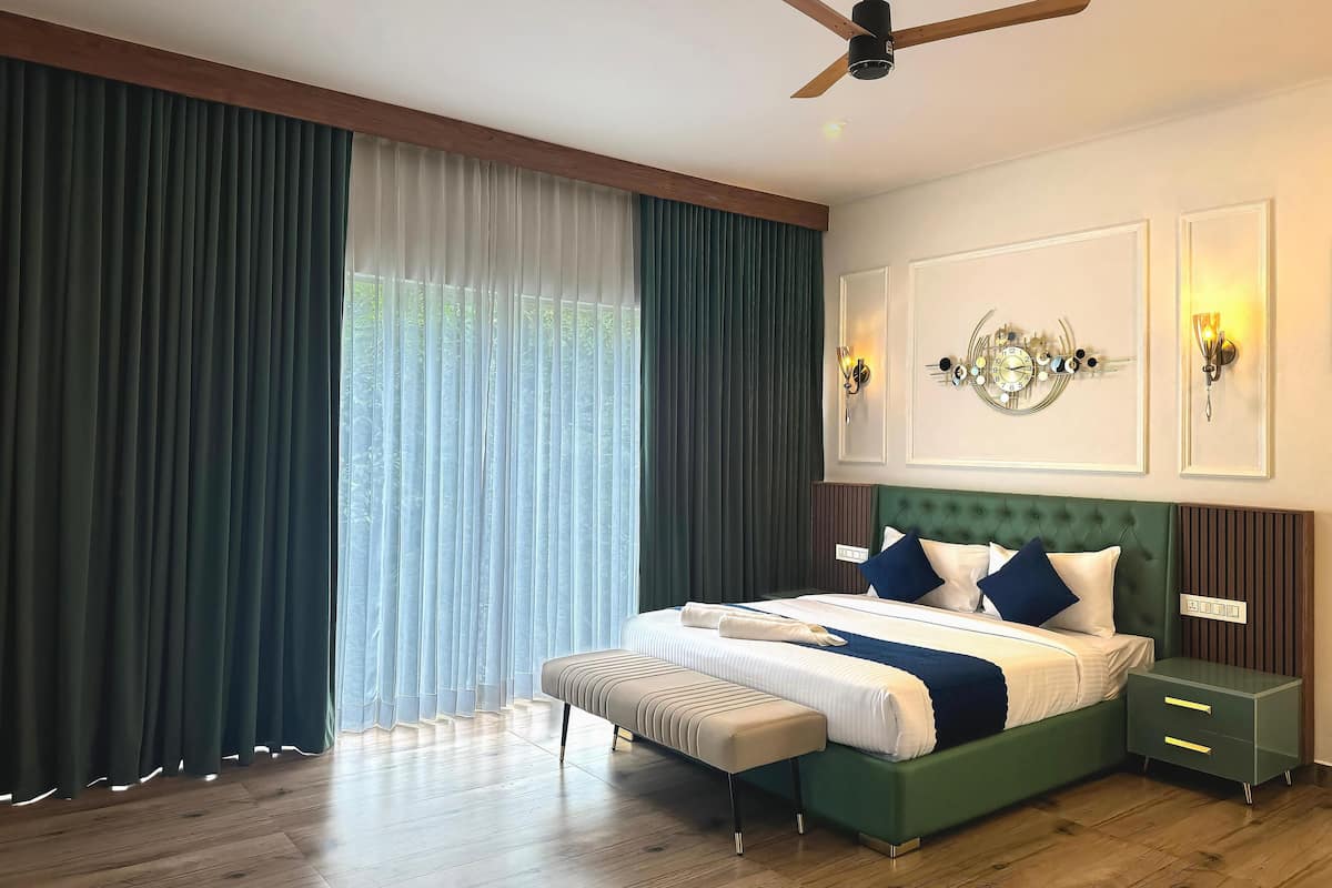Ein modernes Schlafzimmer mit einem mit Stoff bezogenen grünen Bett, Holzboden, Deckenventilator und einem großen Fenster mit durchsichtigen Vorhängen.