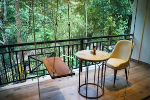 A balcony with a swing, a round table, and a chair, overlooking a forested area. - Hunters Hideout Resort (Vythiri)
