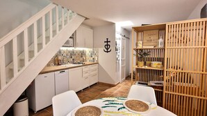 A compact kitchen with white cabinets, a wooden staircase, and a dining area with a table set for two. - Apartment with pool in the Camargue - family time in a great complex (Saint-Laurent-d'Aigouze)