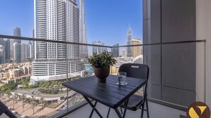 Balcón con mesa, silla y planta en maceta, con vista a un paisaje urbano con edificios altos.