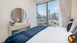 Habitación de hotel con una cama grande, un espejo redondo, una mesita de noche con lámpara y vistas a la ciudad a través de amplios ventanales.