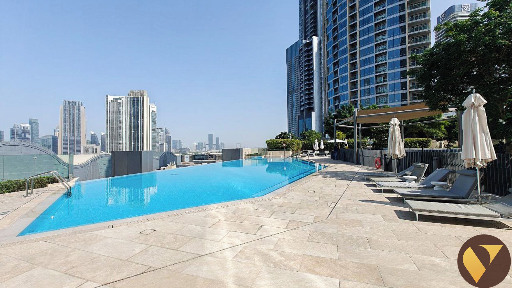 Une piscine sur le toit, avec la vue sur les grat-ciel de la ville en arrière-plan, des chaises longues et des parasols.