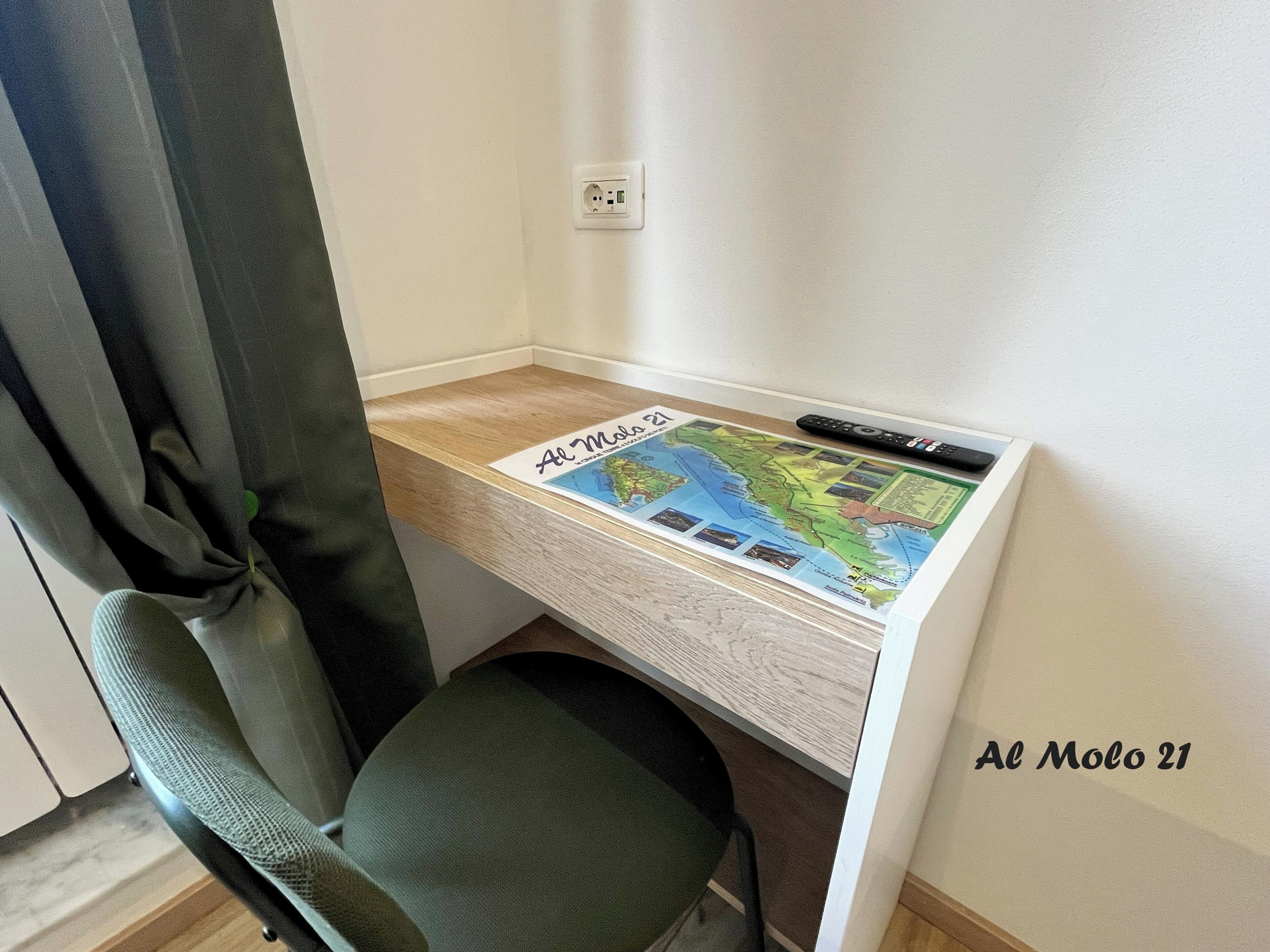 A corner desk with a map, a remote, and a power outlet.