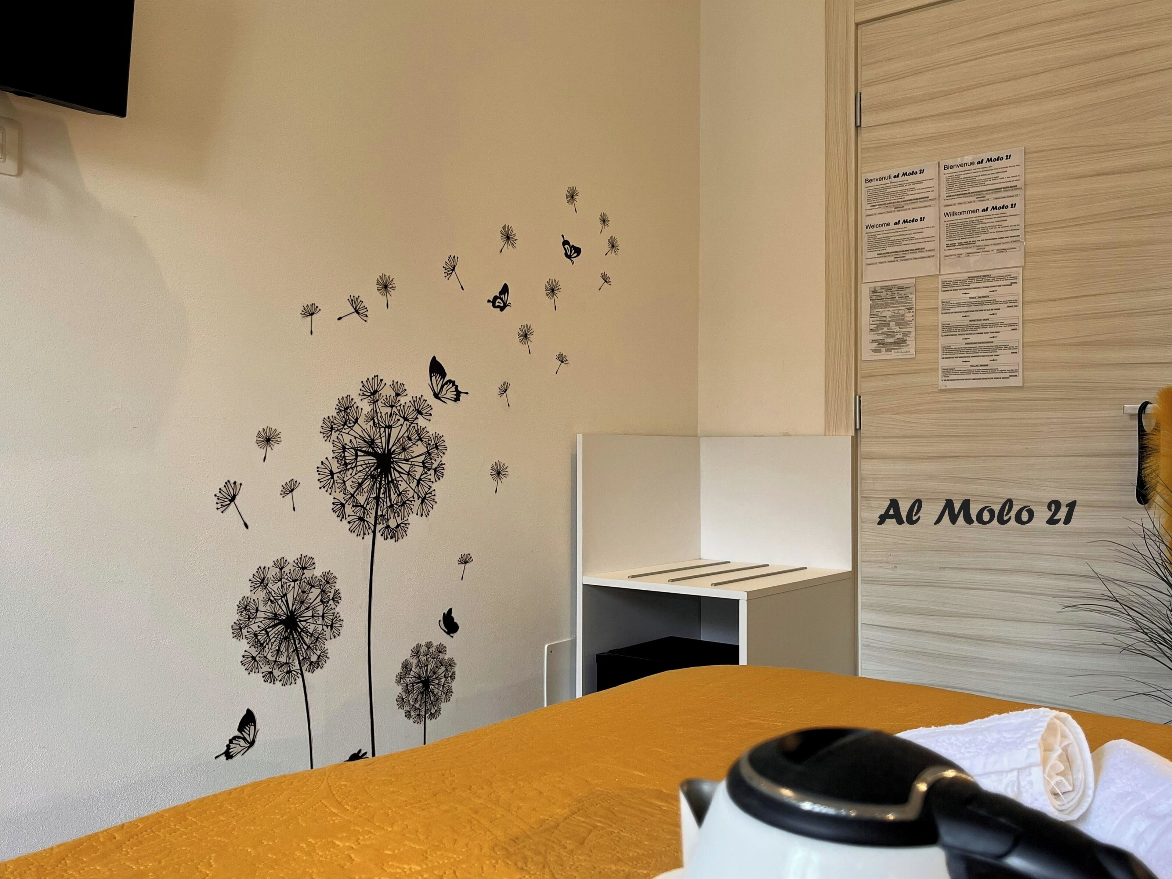 Una habitación con una pared decorada con adhesivos de diente de león y mariposas, una pizarra con texto y un letrero que dice 'Al Molo 21'.