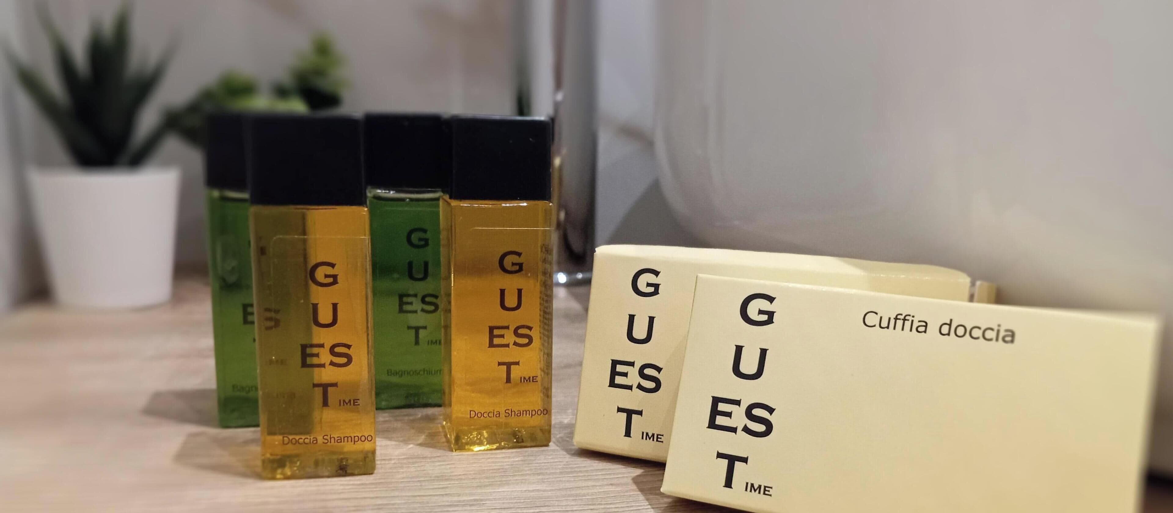 Un conjunto de artículos de aseo que incluye una botella verde, una amarilla y una caja blanca con la etiqueta 'Cuffia doccia' sobre una superficie de madera.