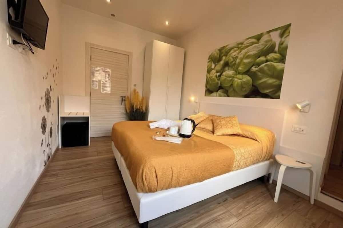 Quarto com uma cama, uma mesinha, uma televisão, um quadro e uma porta.