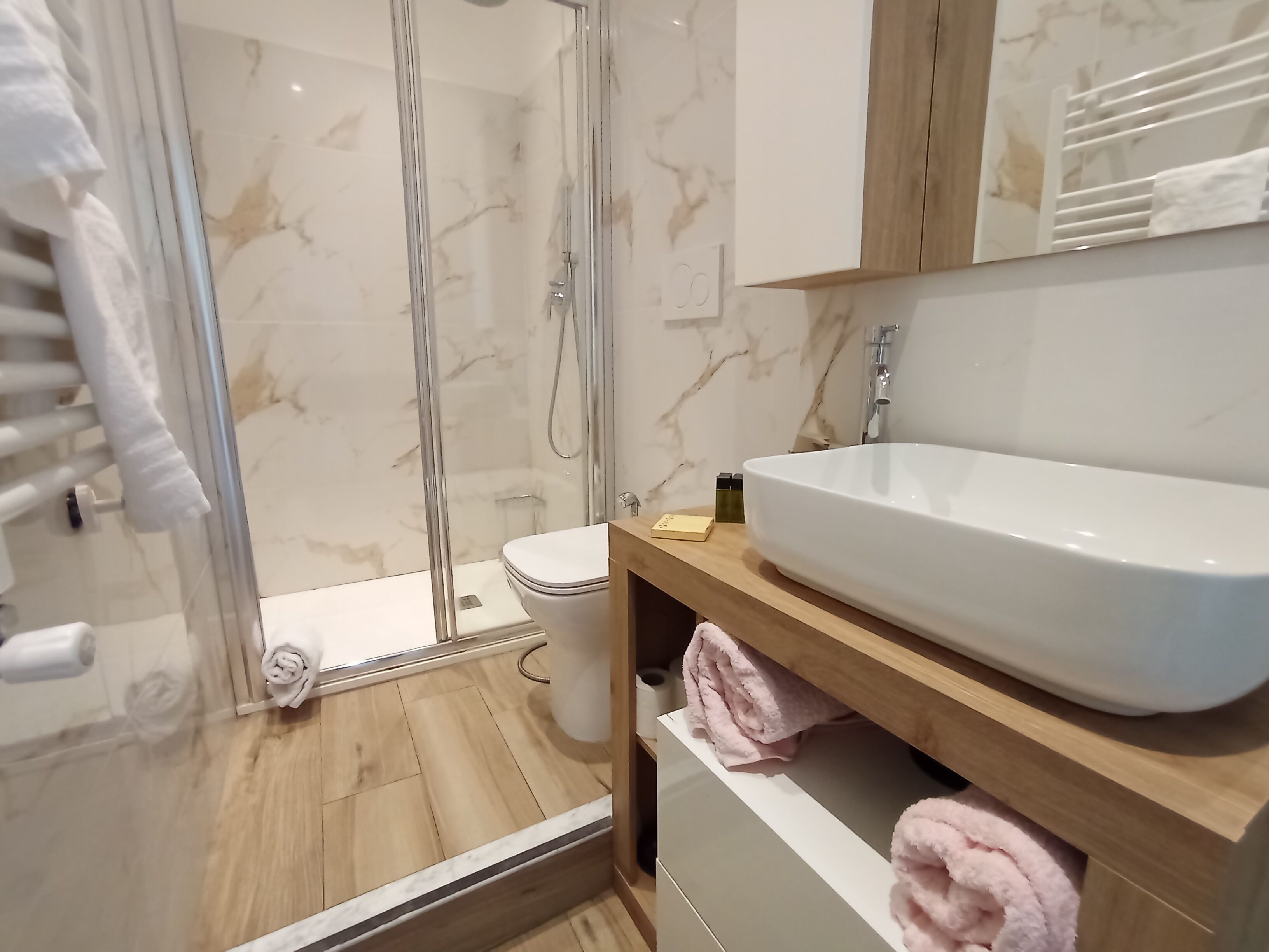 A modern bathroom with a glass-enclosed shower, a white sink, and a wooden vanity.