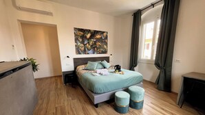 A bedroom with a bed, bedside tables, a desk, a window with curtains, and a wall-mounted air conditioner. - al molo 21 (La Spezia)