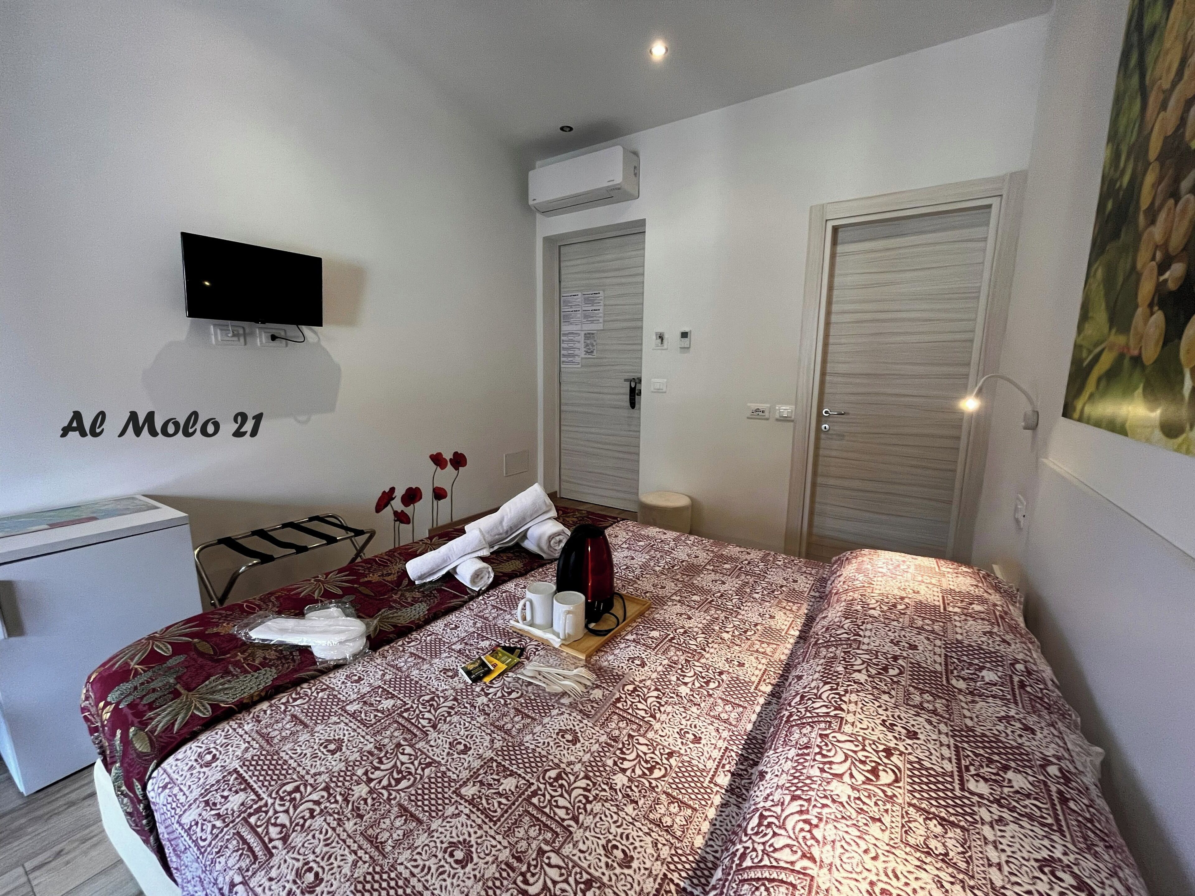 A hotel room with a bed, a desk, a TV, a wardrobe, and a painting on the wall.