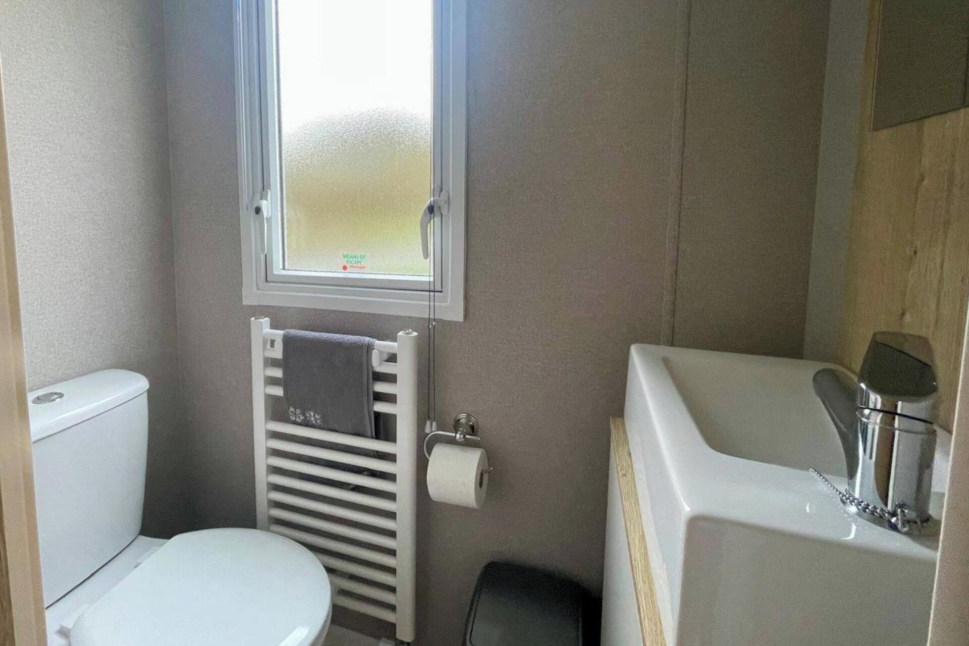 A compact bathroom with a toilet, a towel rack, a window, and a sink.