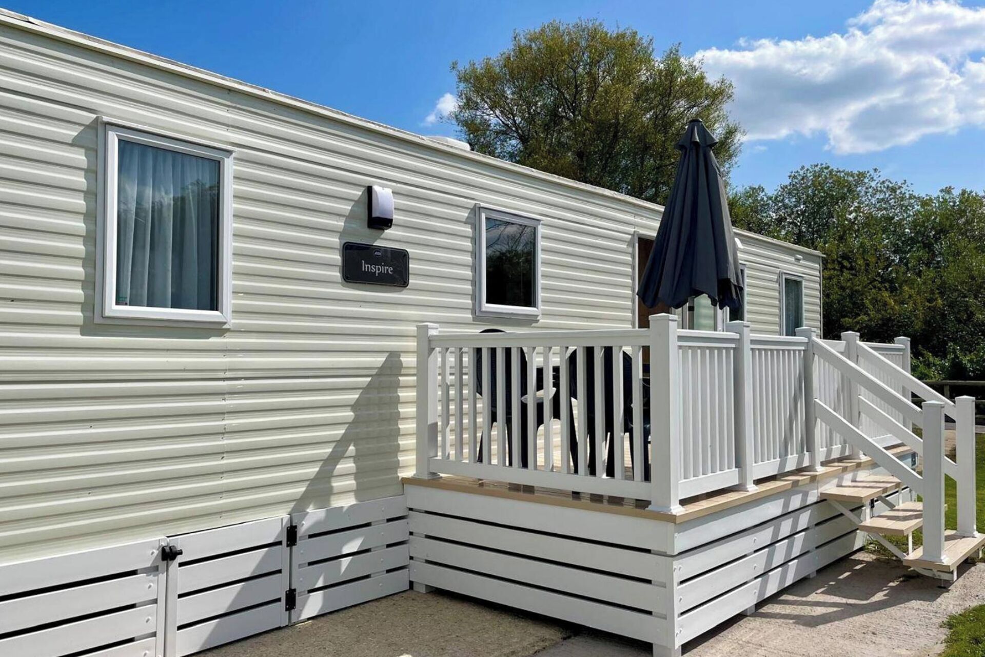 A mobile home with a white exterior, a deck with a railing, and a small window.