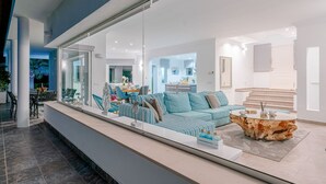 Een moderne woonkamer met een glazen scheiding, een blauw gestreept bankstel, een ronde salontafel en een trap die naar een hoger niveau leidt.