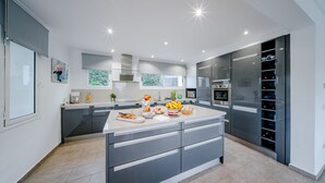 Een moderne keuken met grijze kastjes, een groot eiland en roestvrijstalen apparatuur.