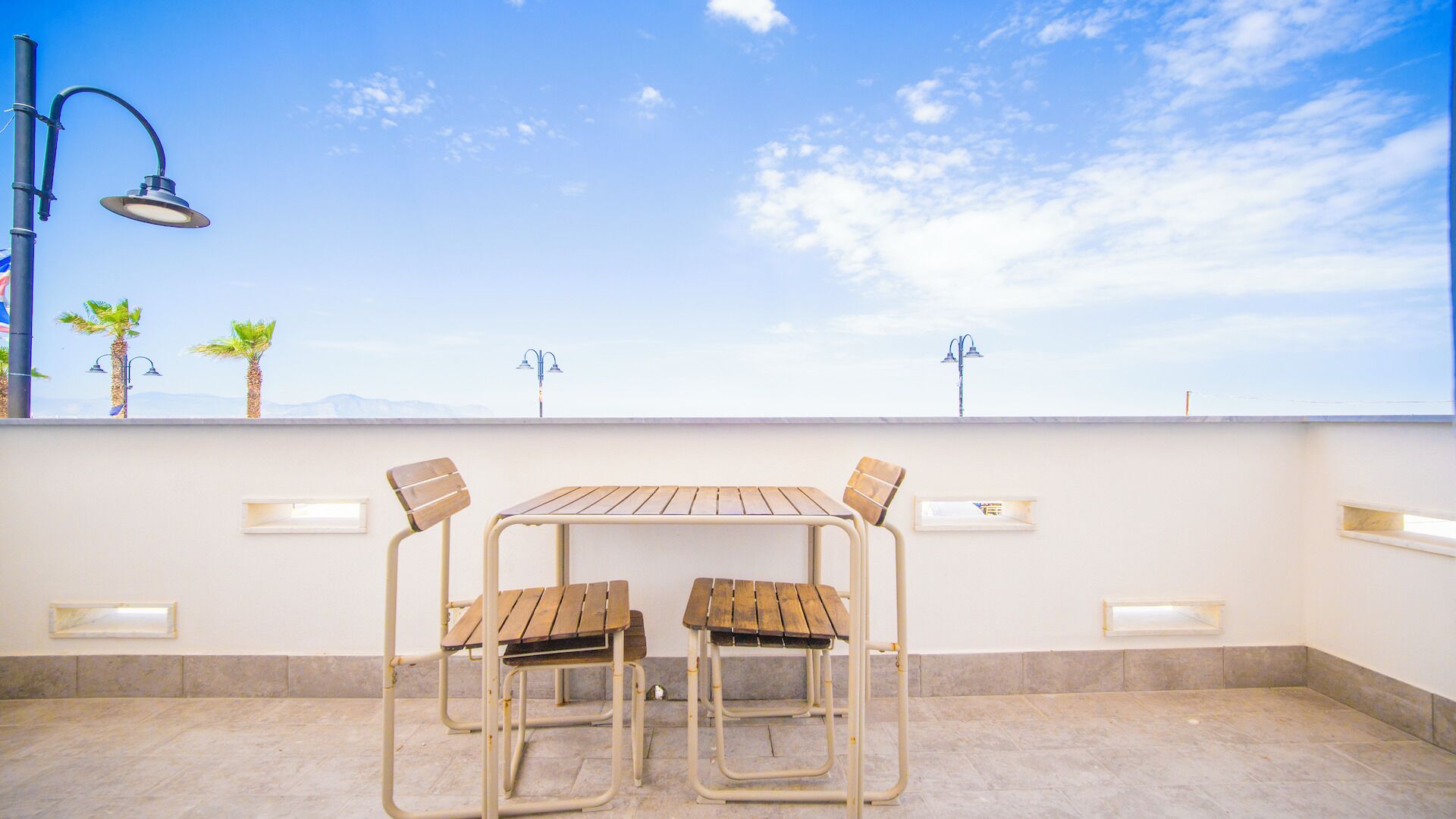 A rooftop terrace with a table and chairs, outdoor lighting, and a view of the sky and mountains.